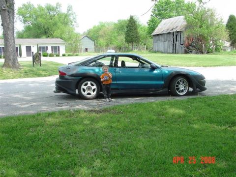 1993 Ford Probe - A teal 1993 Ford Probe with a body kit is parked outside a barn.
