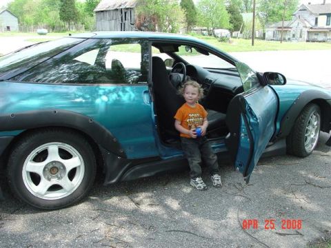 1993 Ford Probe - A child sits in the open door of a teal 1993 Ford Probe, which has aftermarket fender flares.
