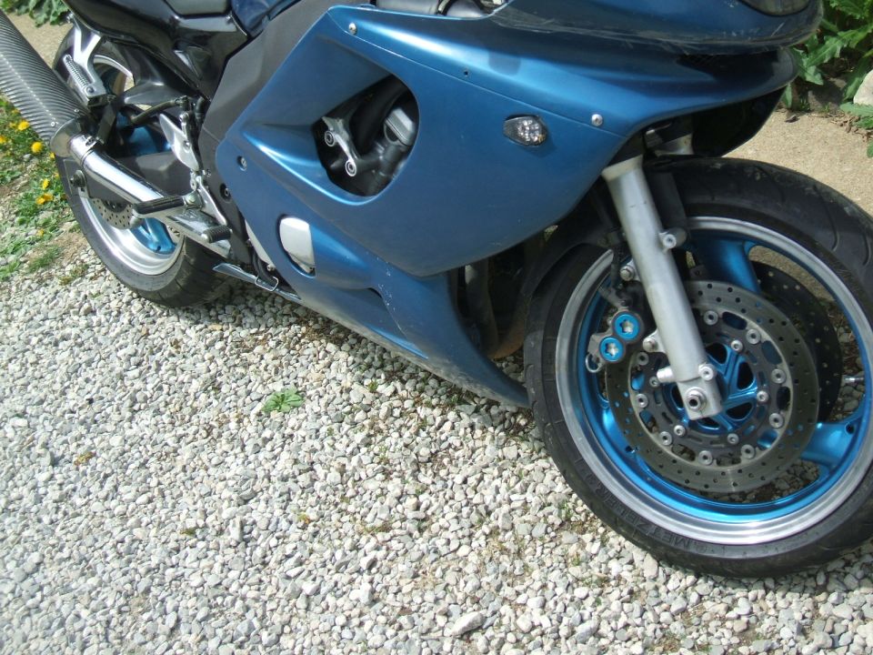 Blue motorcycle front wheel and fairing, parked on gravel
