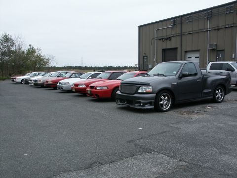 2001 Mercury Grand Marquis - A line of Ford Mustangs and a dark gray Ford F-150 SVT Lightning pickup truck are parked outside a building.