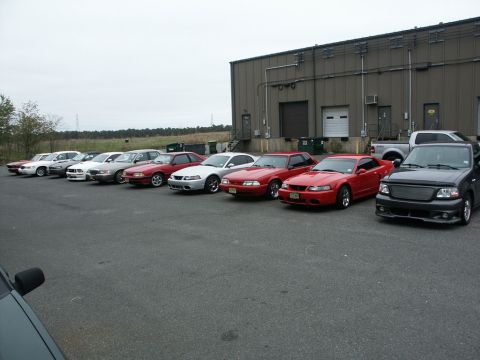 2001 Mercury Grand Marquis - Several Ford Mustangs and a Ford F-150 are lined up in a parking lot in front of a large industrial building.
