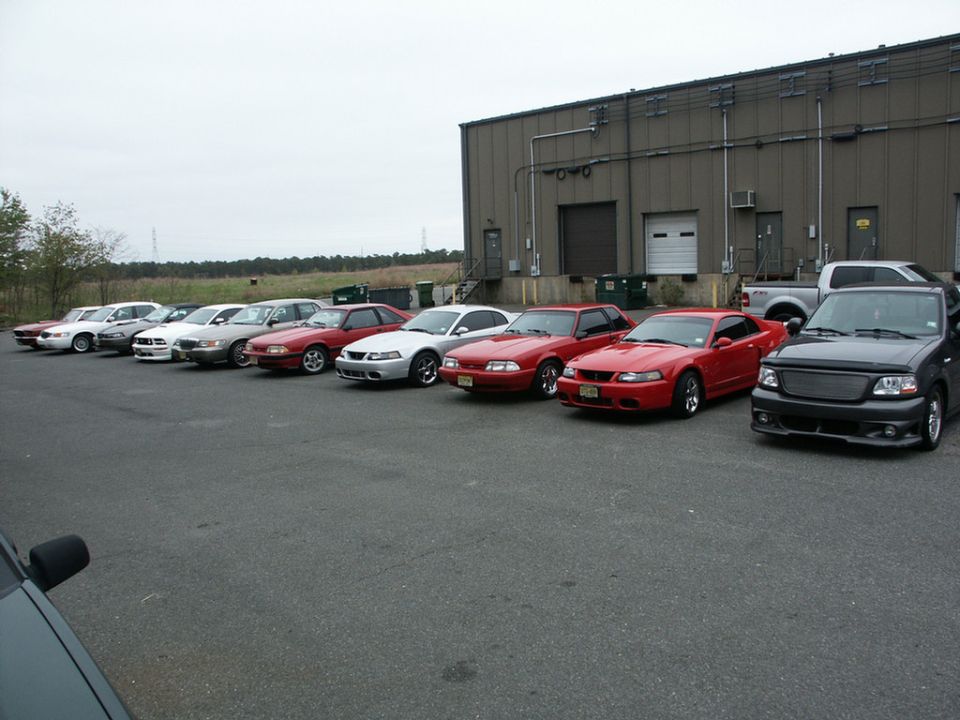 Line of red Ford Mustangs and a black Ford F-150 parked outside a building