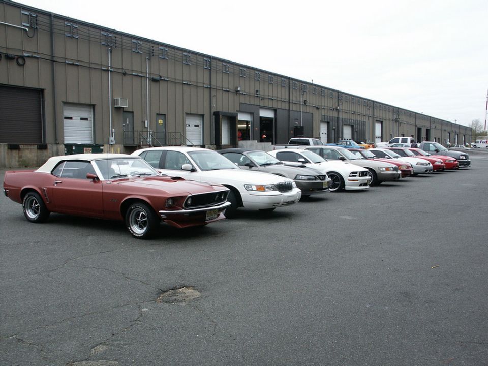Red 1969 Ford Mustang convertible and other cars parked in a row outside a warehouse