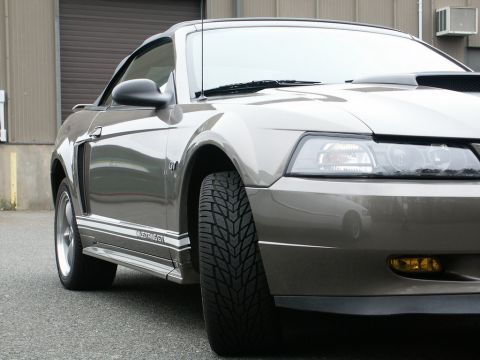2001 Mercury Grand Marquis - A gray Ford Mustang GT is parked in front of a garage door, showing its front quarter panel and wheel.