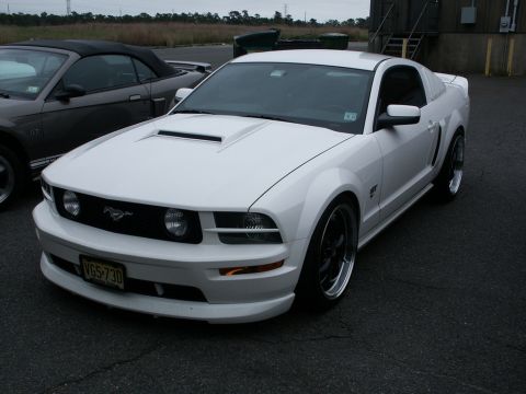 2001 Mercury Grand Marquis - A white Ford Mustang is parked on asphalt next to a dark convertible, with a building in the background.