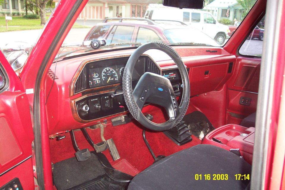 Red Ford truck interior with black laced steering wheel and wood-grain dash