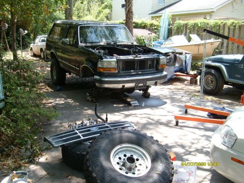 1992 Ford Bronco - A black 1992 Ford Bronco is undergoing maintenance, with its hood open and front wheels removed.