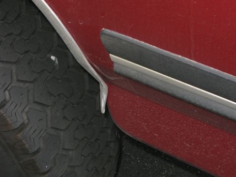 1991 Ford F-150 - Close-up view of the fender trim and tire on a red vehicle, showing a detail of the bodywork.