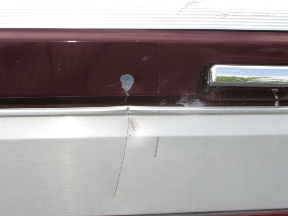 Maroon and silver truck bumper with dent and paint chip. Chrome trim visible