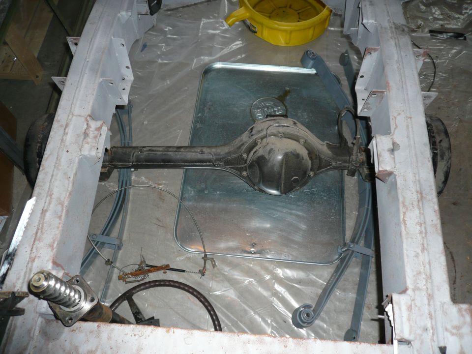 Bare solid rear axle on leaf springs inside a stripped gray ladder frame during a rebuild