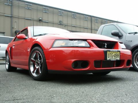 2001 Mercury Grand Marquis - A red 2001 Ford Mustang Cobra is parked next to a pickup truck, showing its front grille and chrome wheels.