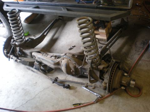 1993 Ford Bronco - Disassembled front axle and suspension parts are laid out on a concrete floor.