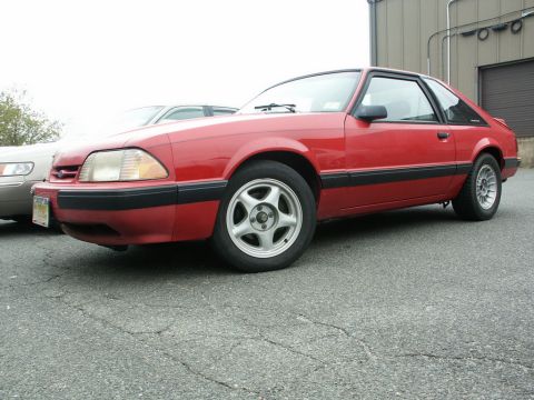 2001 Mercury Grand Marquis - A red coupe with black trim is parked next to another vehicle. The car is viewed from the front three-quarter angle.
