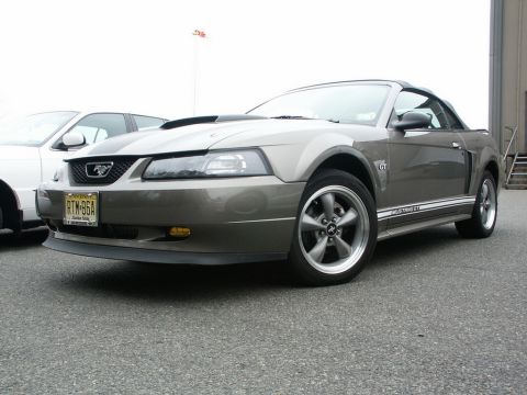 2001 Mercury Grand Marquis - A gray Ford Mustang GT convertible is parked on asphalt, with another vehicle to its left.