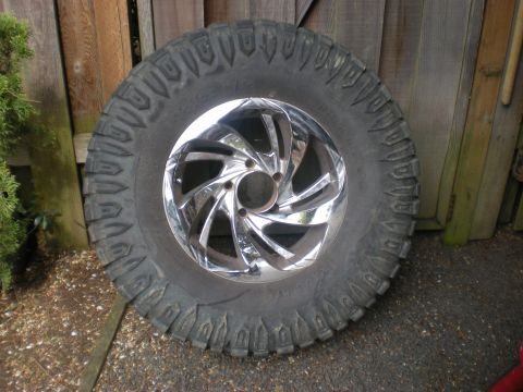 1993 Ford Bronco - A single tire and chrome wheel are shown against a weathered wooden fence.