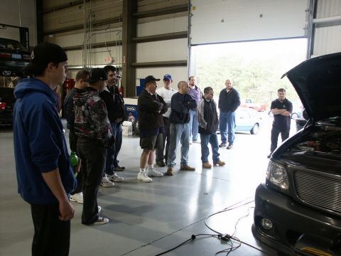 2001 Mercury Grand Marquis - A group of people observe a truck with its hood open in a garage setting, possibly for a performance event.