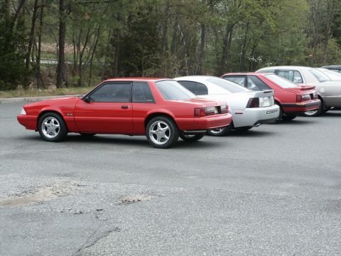 2001 Mercury Grand Marquis - A red 1987 Ford Mustang coupe is parked in a line with other vehicles.
