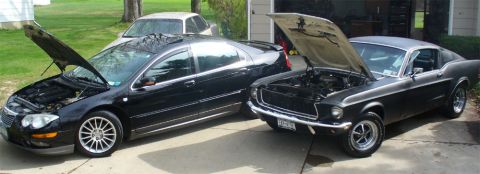 2002 Chrysler 300M - Two cars, a Chrysler sedan and a classic Mustang, are parked side-by-side with their hoods open.