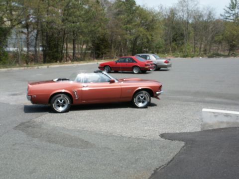 2001 Mercury Grand Marquis - A classic orange convertible is parked in a lot with other cars in the background.