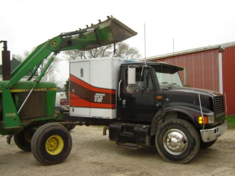 1992 Ford Bronco - A black International truck is connected to a white box trailer and a green tractor loader.