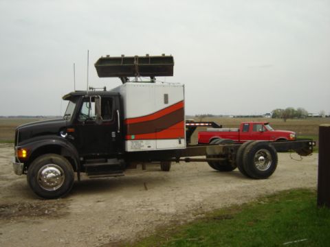 1992 Ford Bronco - A black semi-truck is shown from the side, carrying a red pickup truck on its chassis in an outdoor setting.