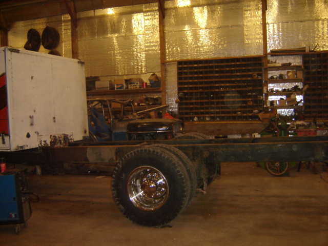 Truck chassis with dual rear wheels, box body on front, in a workshop with shelves of parts