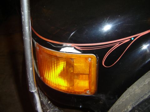 1992 Ford Bronco - Close-up of a black vehicle's front corner, showing an orange turn signal and decorative pinstripes.