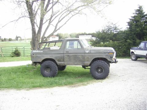 1978 Ford Bronco - This lifted 1978 Ford Bronco features flame decals and a roll cage, parked next to another vehicle.