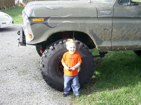 1978 Ford Bronco - A young child stands next to the massive tire of a lifted 1978 Ford Bronco, highlighting its impressive size.