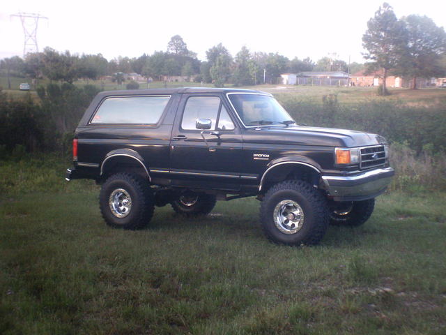 Lifted black Ford Bronco SUV with large off-road tires and chrome wheels parked on grass