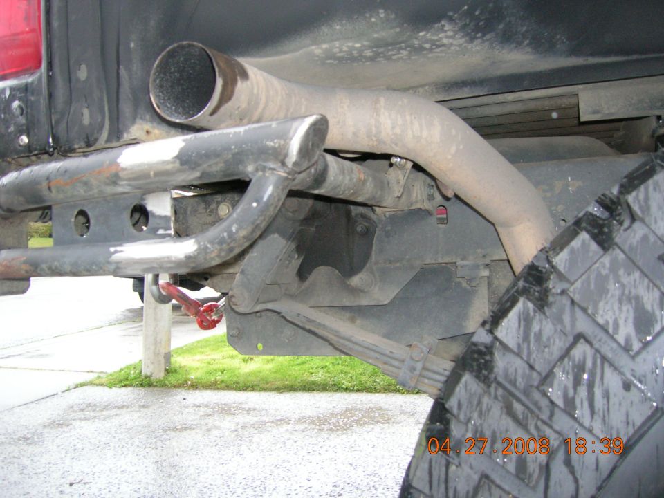Side-exit exhaust stack, tube bumper, leaf springs and mud tire under a lifted black truck
