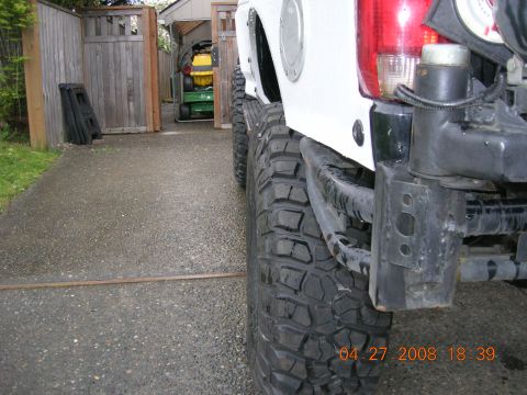 1996 Ford Bronco - Rear view of a white SUV's bumper and tire, parked on a wet driveway.