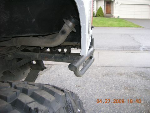 1996 Ford Bronco - Close-up view of the rear bumper and exhaust system of a vehicle, with a prominent tire in the foreground.