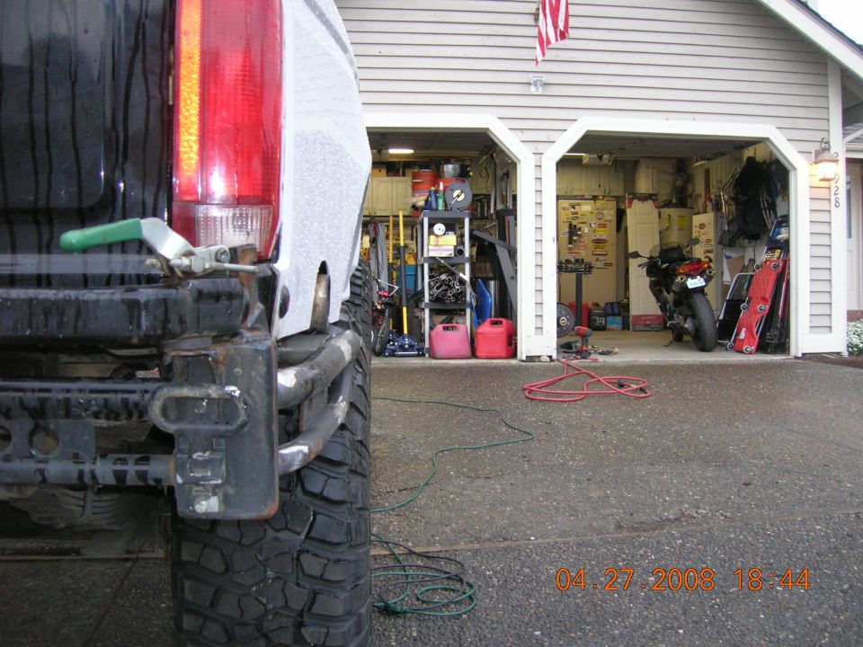 Rear corner of lifted black truck with primered quarter panel and tube rear bumper in driveway