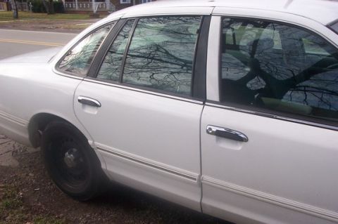 1996 Ford Crown Victoria - Side view of a white sedan with chrome trim and door handles, reflecting bare tree branches.