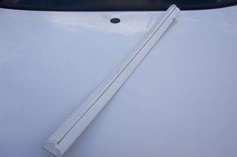 1996 Ford Crown Victoria - A white trim piece lies on the hood of a white car, with a black circular object visible in the background.