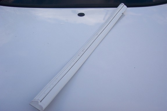 White trim piece on a white car hood, with a black circular object visible behind it