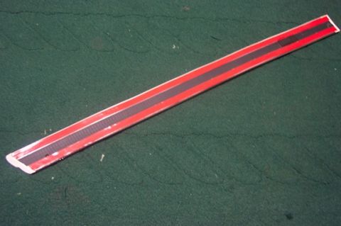 1996 Ford Crown Victoria - A red and black trim piece with a textured black stripe is shown against a green background.