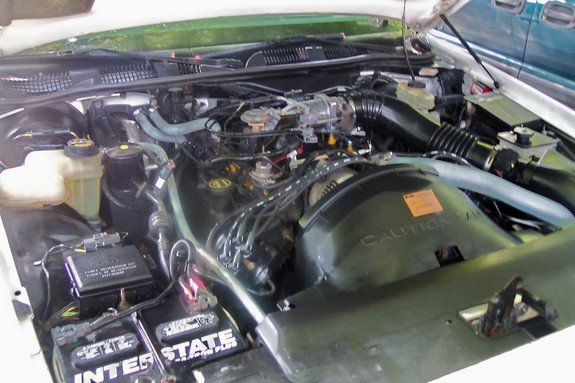 Engine bay with visible batteries and hoses. Caution label on fan shroud