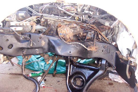 Vehicle frame with engine parts, hoses, and wiring. Some rust is visible