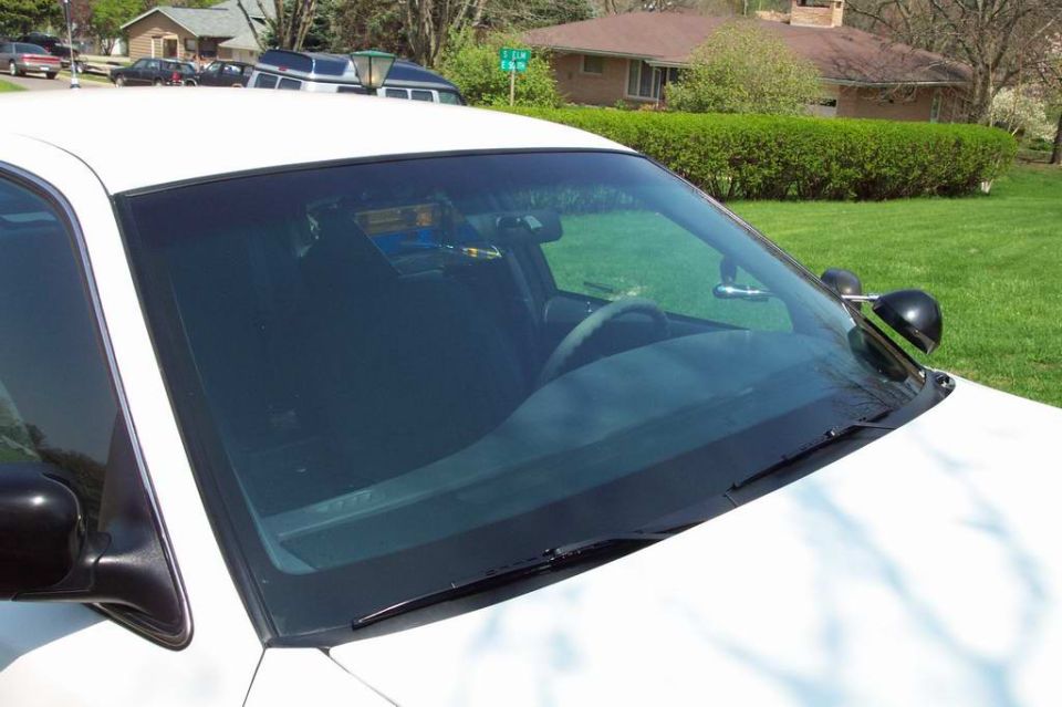 Windshield and cowl of a white sedan with spotlight, viewed across the hood