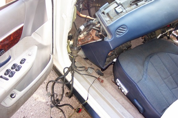 Car interior disassembled, showing door panel, seat, and dashboard components with exposed wiring