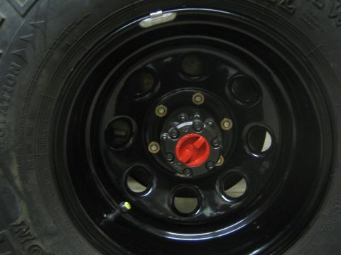 1987 Suzuki Samurai - Close-up of a vehicle's wheel hub and tire, showing a red hubcap and black rim.