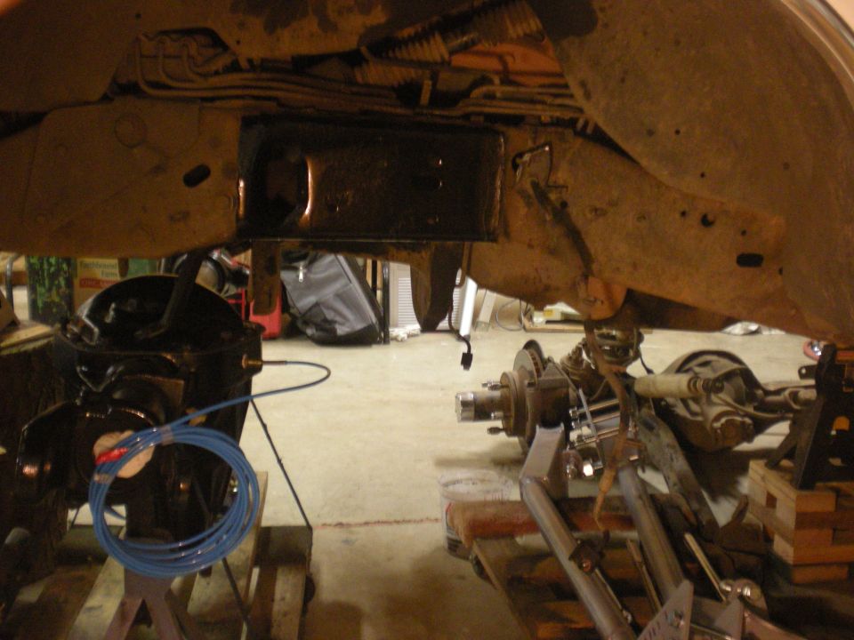 Underbody view of vehicle frame with suspension parts removed and on stands. Blue tubing is visible