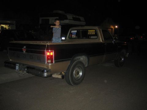 1999 Ford F-250 - A young boy stands in the bed of a classic Dodge pickup truck at night, with the 'DODGE' lettering visible on the tailgate.