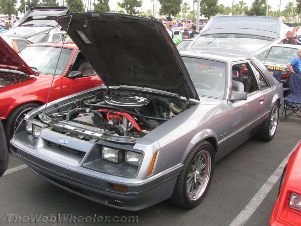 Silver 1980s Ford Mustang GT with hood open, parked next to a red car