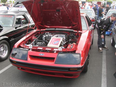 1968 Ford Mustang - A red Ford Mustang is displayed with its hood open, revealing the engine compartment and a Ford logo sign.