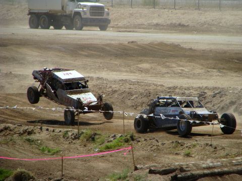 2008 Ford Bronco - Off-road buggies compete on a dirt track, with one vehicle jumping over a mound.