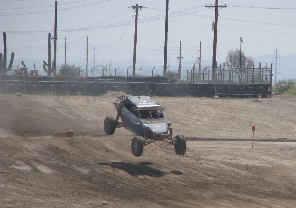 Off-road buggy mid-air over dirt track, blue and silver body, roll cage visible