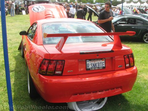 1968 Ford Mustang - Red Ford Mustang with a large rear spoiler is parked on grass at an outdoor car show.